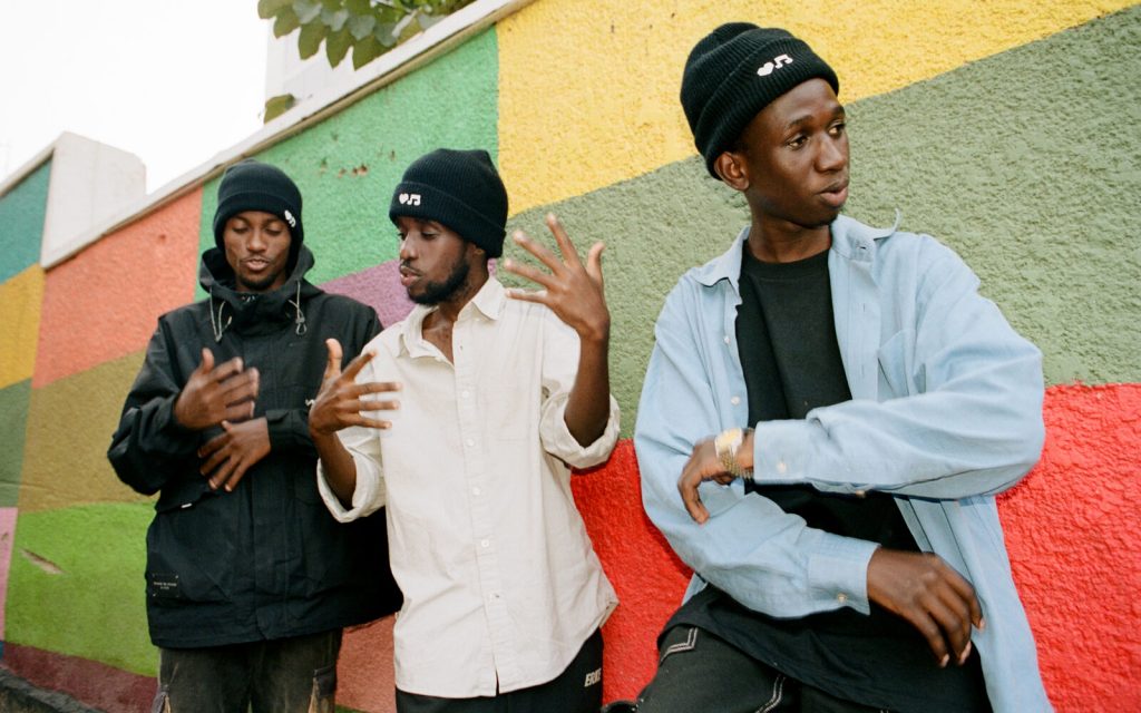 Three musicians talking in front of a colorful wall