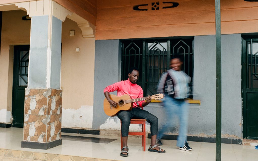 A seated guitarist with a person moving past in the foreground