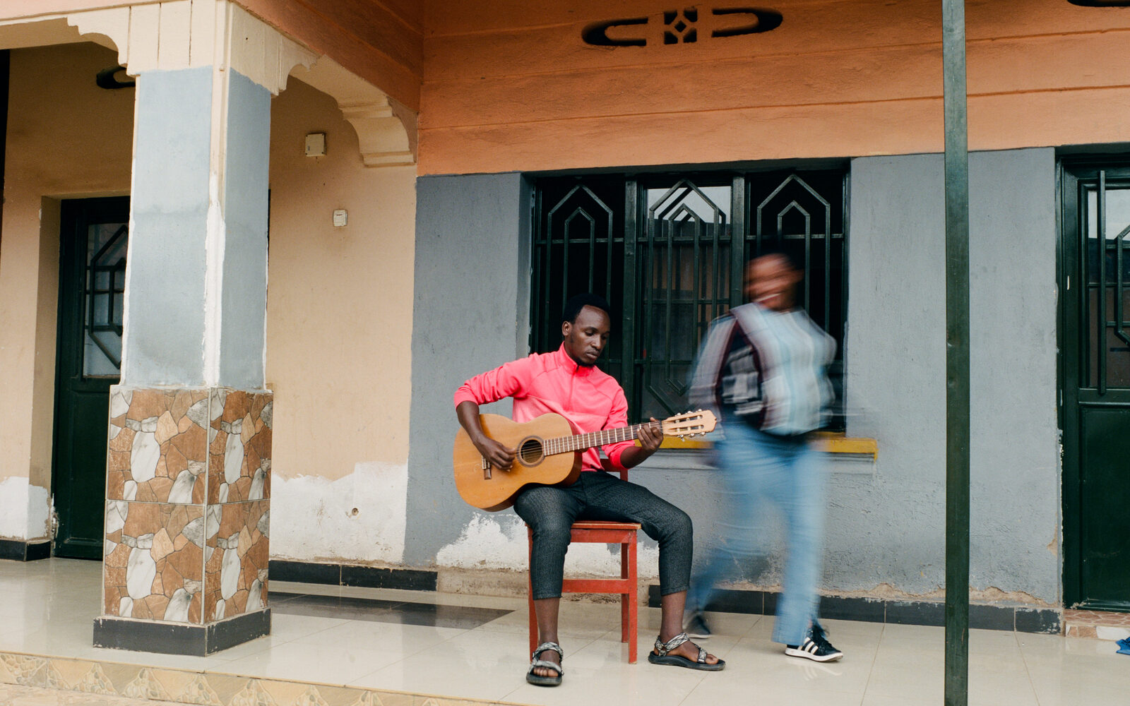 A seated guitarist with a person moving past in the foreground